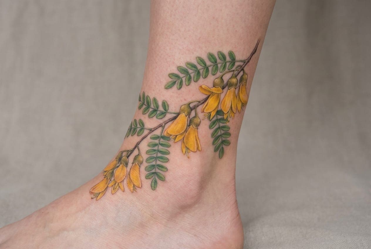 Colour tattoo of yellow kōwhai flowers wrapping around an ankle